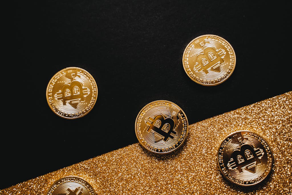 Stylish arrangement of golden Bitcoin coins on a sparkling gold glitter and black background.