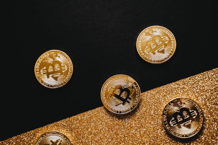 Stylish arrangement of golden Bitcoin coins on a sparkling gold glitter and black background.