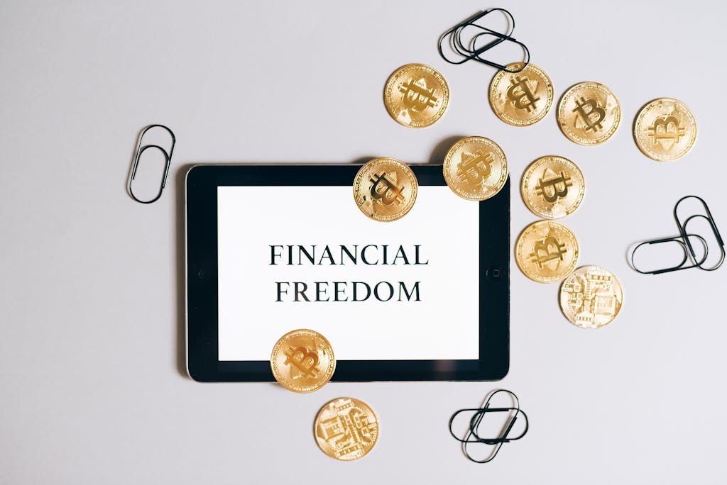 Top view of a tablet displaying 'Financial Freedom' with scattered bitcoin coins, symbolizing digital currency.
